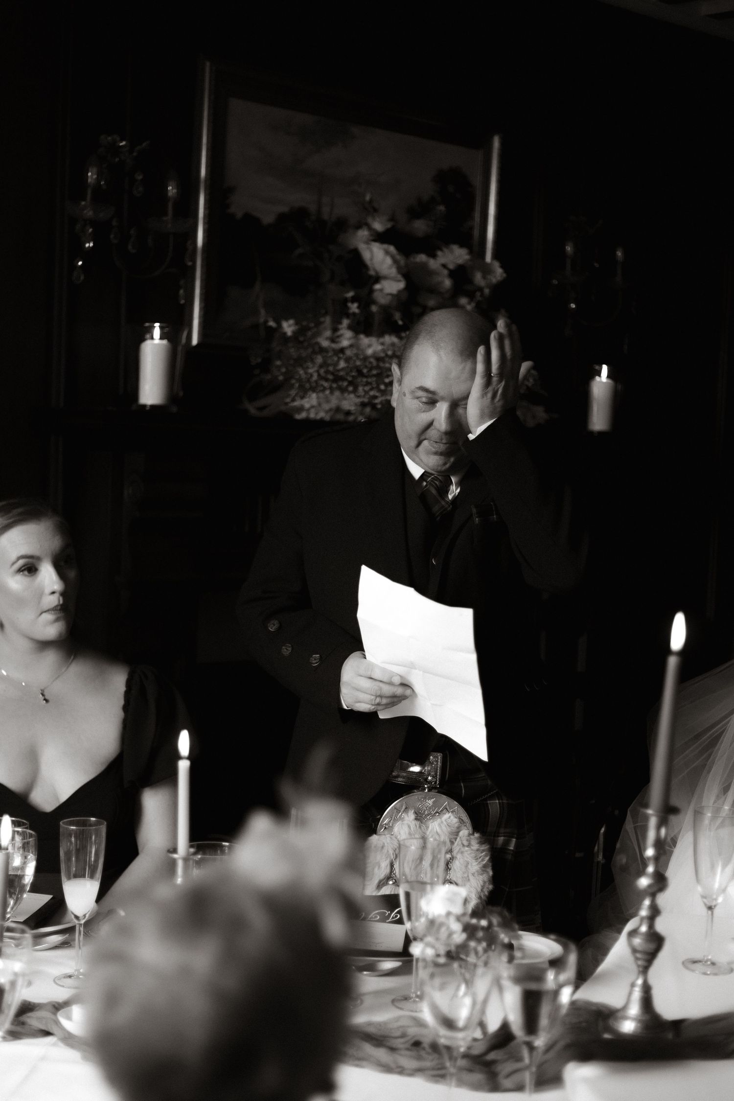 Black and white candid reception scene with guests seated at tables illuminated by candlelight.