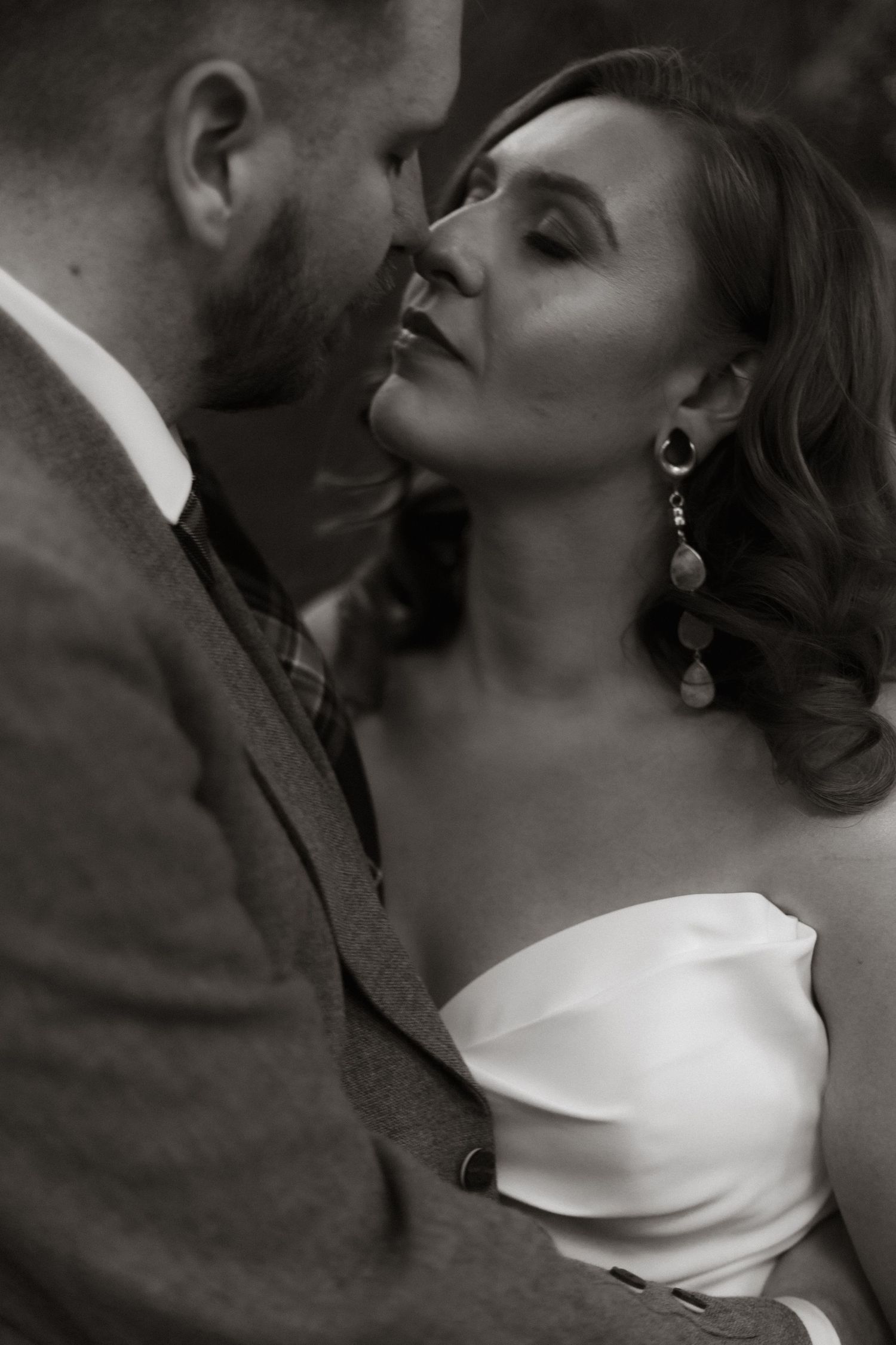 Black and white romantic close-up of couple in intimate moment, with woman wearing elegant one-shoulder dress.