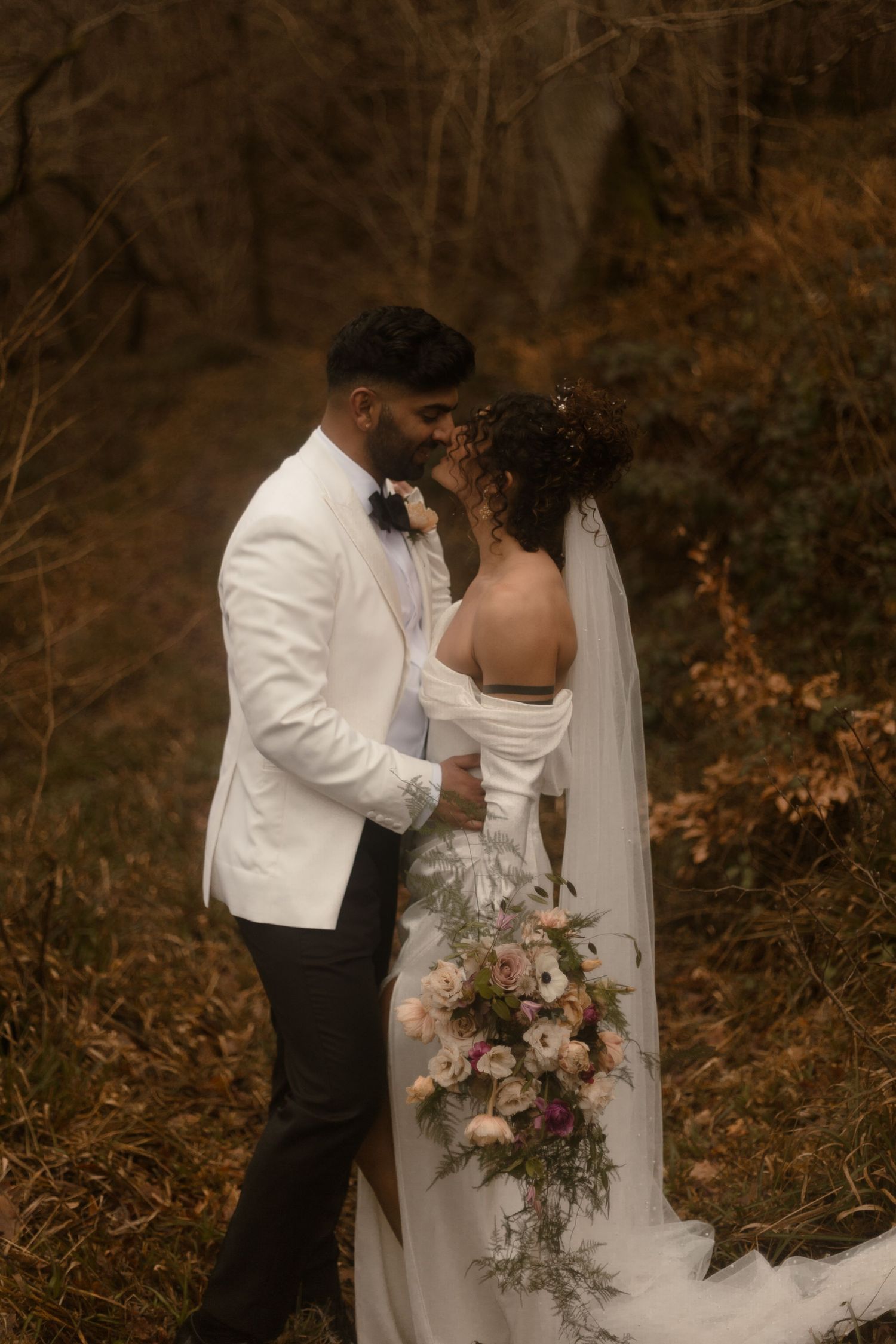 A romantic fall wedding photograph featuring a couple embracing in white attire against a backdrop of autumn foliage.