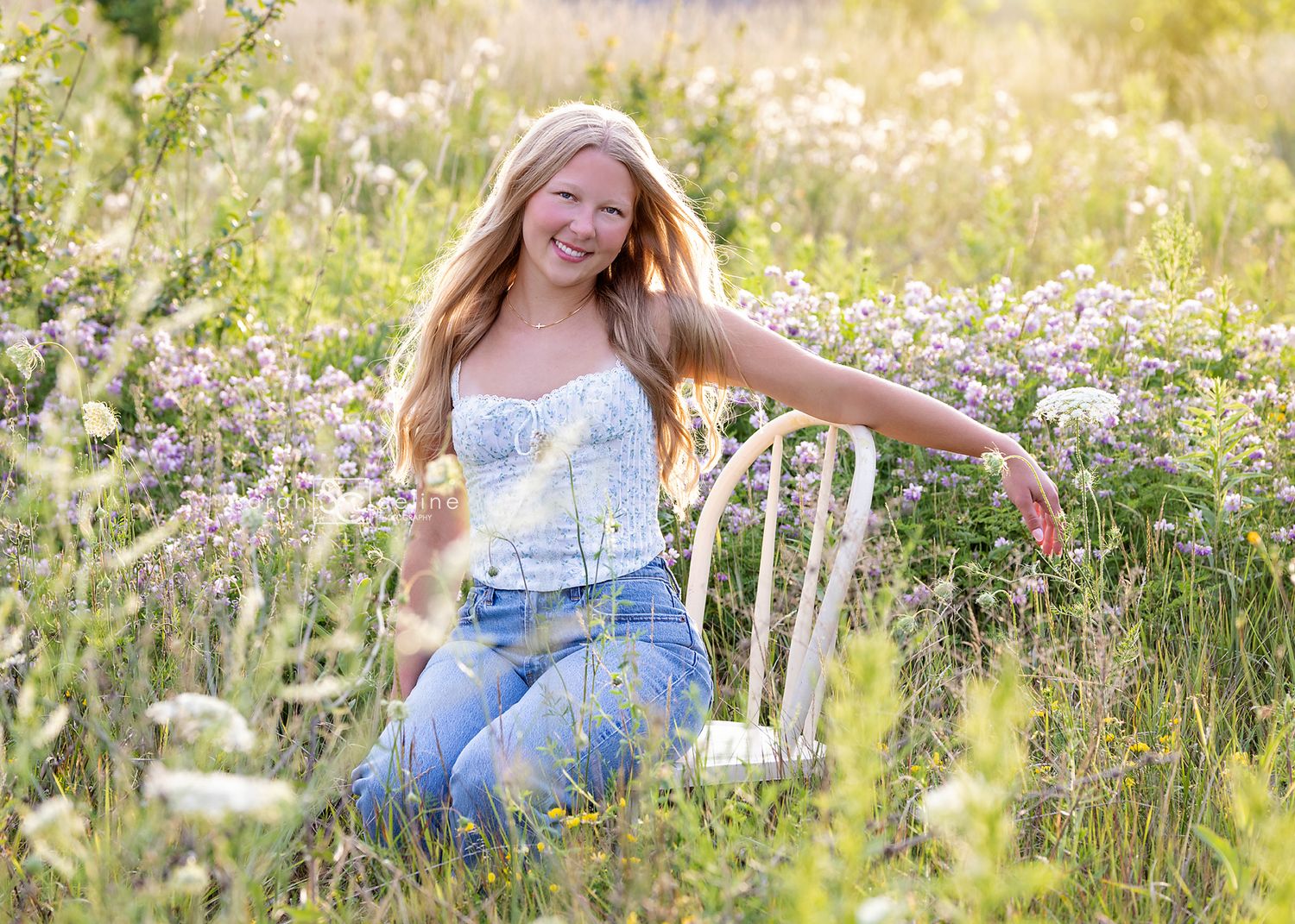 Person in a blue dress laughs while sitting in a wildflower meadow during golden hour sunset.