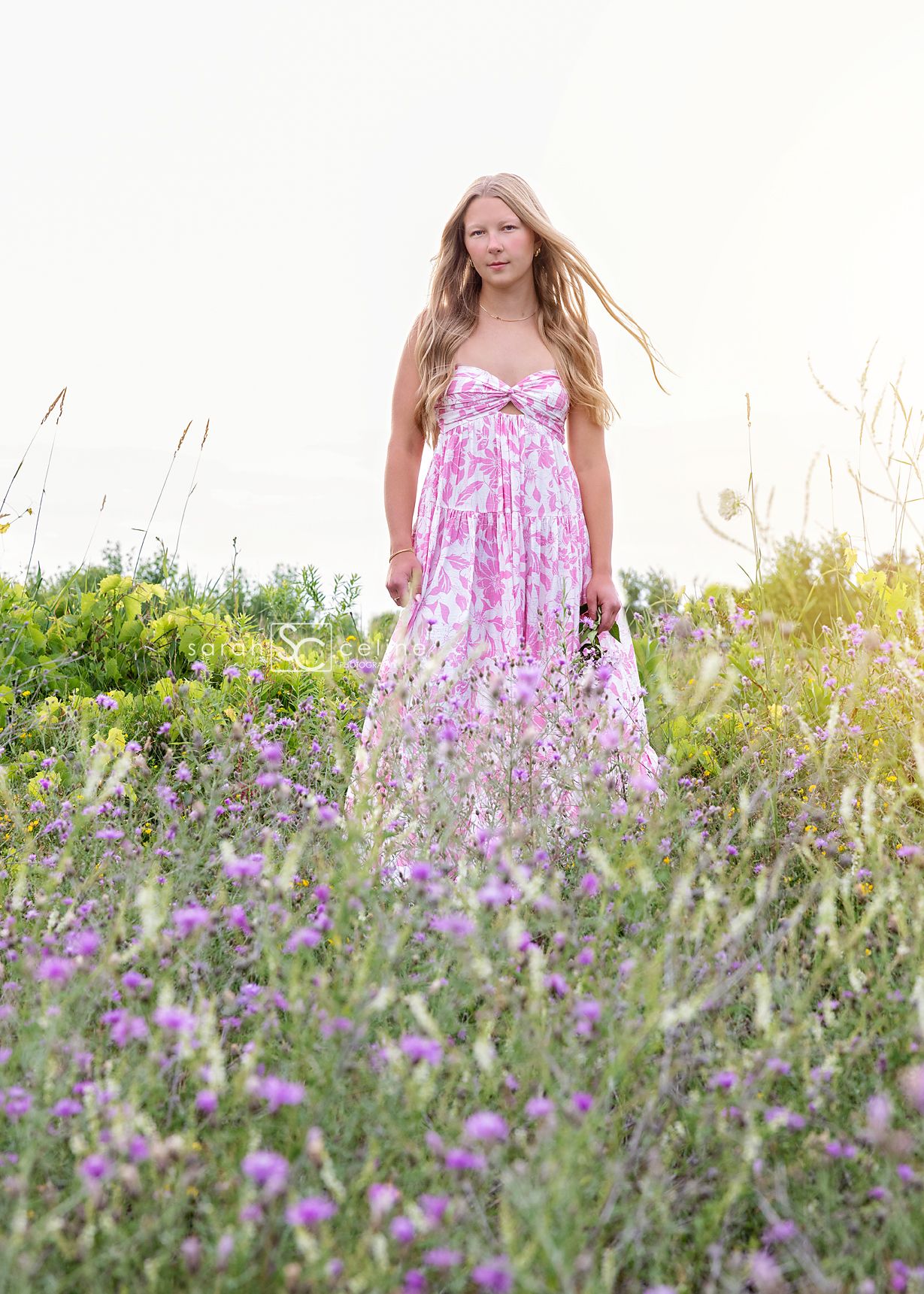 A panoramic shot of someone standing in a meadow of purple wildflowers at sunset with a pink floral dress.