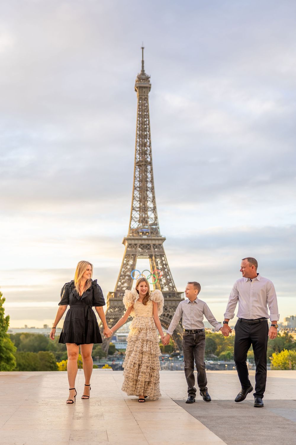 Family holding hands while walking along Trocadero Plaza with iconic Eiffel Tower in background during golden hour.