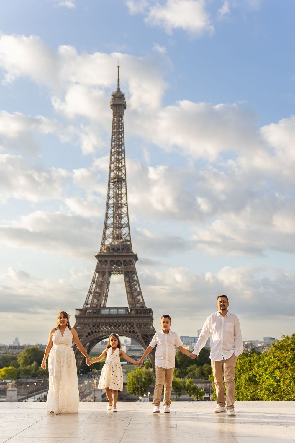 Family photoshoot sequence at Trocadero with the Eiffel Tower in Paris against a blue cloudy sky.
