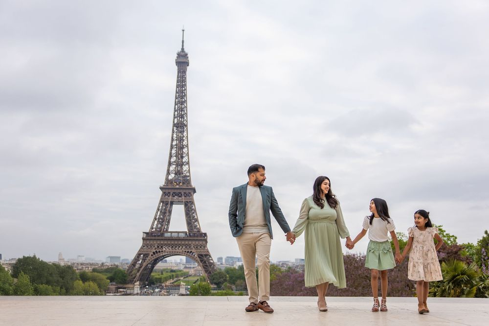 A family holding hands strolls along the Trocadero plaza with the iconic Eiffel Tower in the background on a cloudy day in Paris.