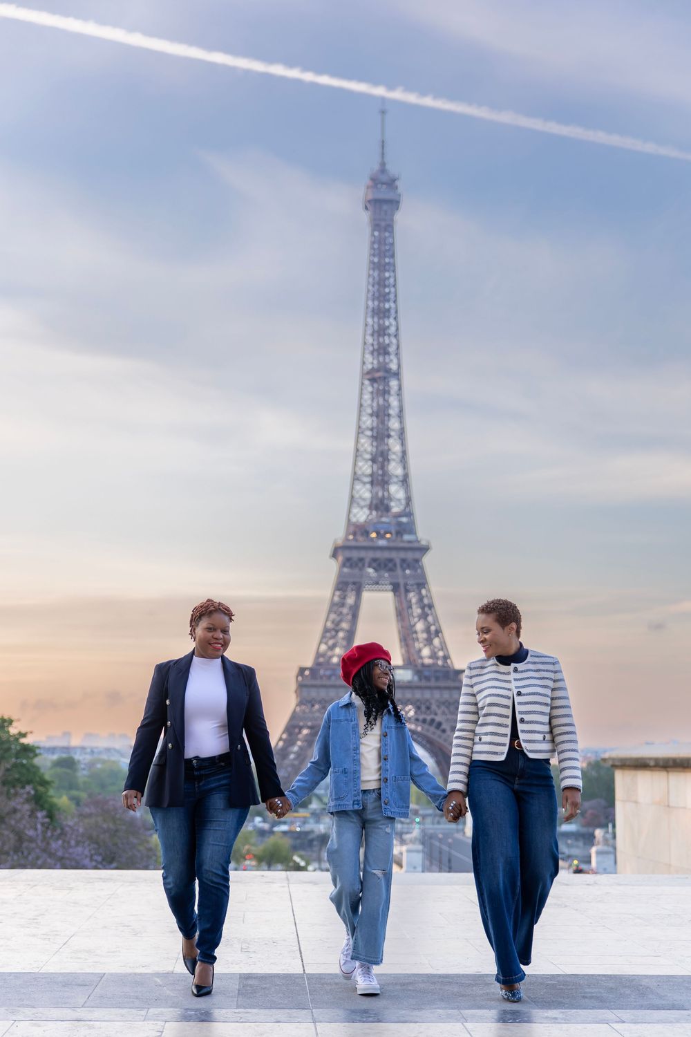 Three people walking together with the Eiffel Tower in Paris visible behind them during sunset.