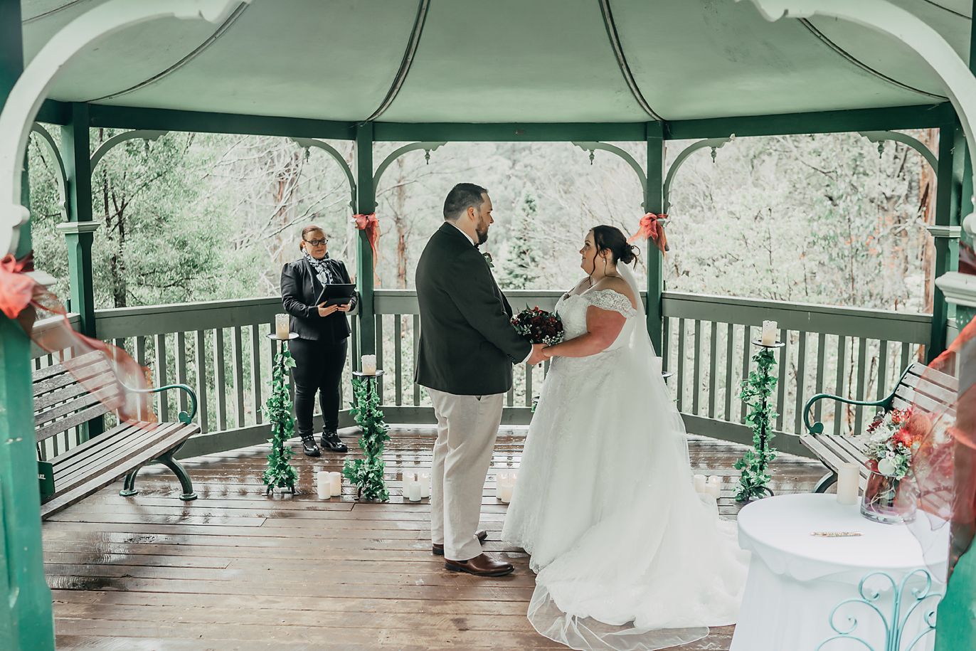 A couple celebrates their wedding ceremony in a green-painted gazebo decorated with pink accents during springtime.
