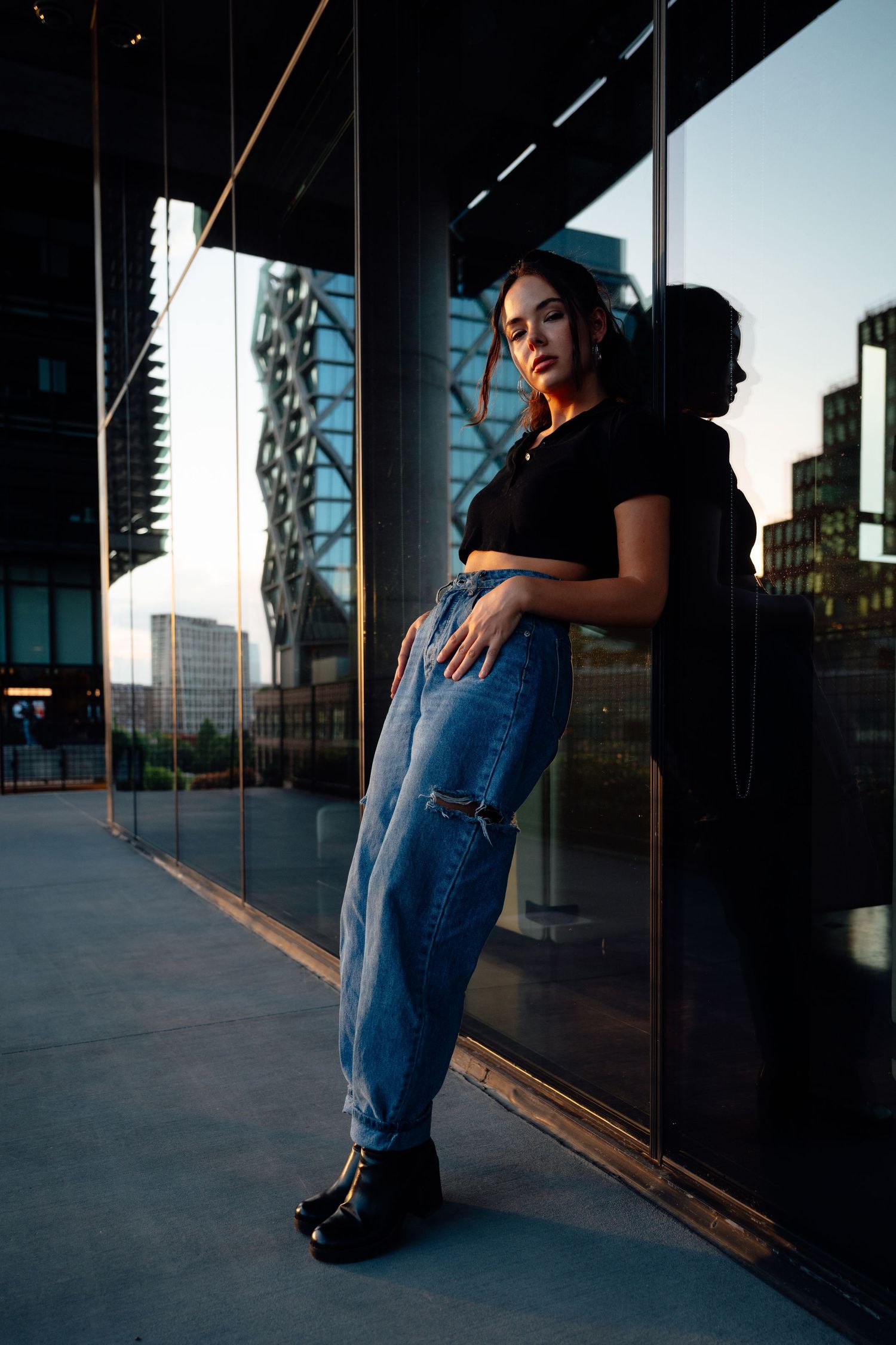 Artistic portrait against reflective glass windows in urban setting at dusk.