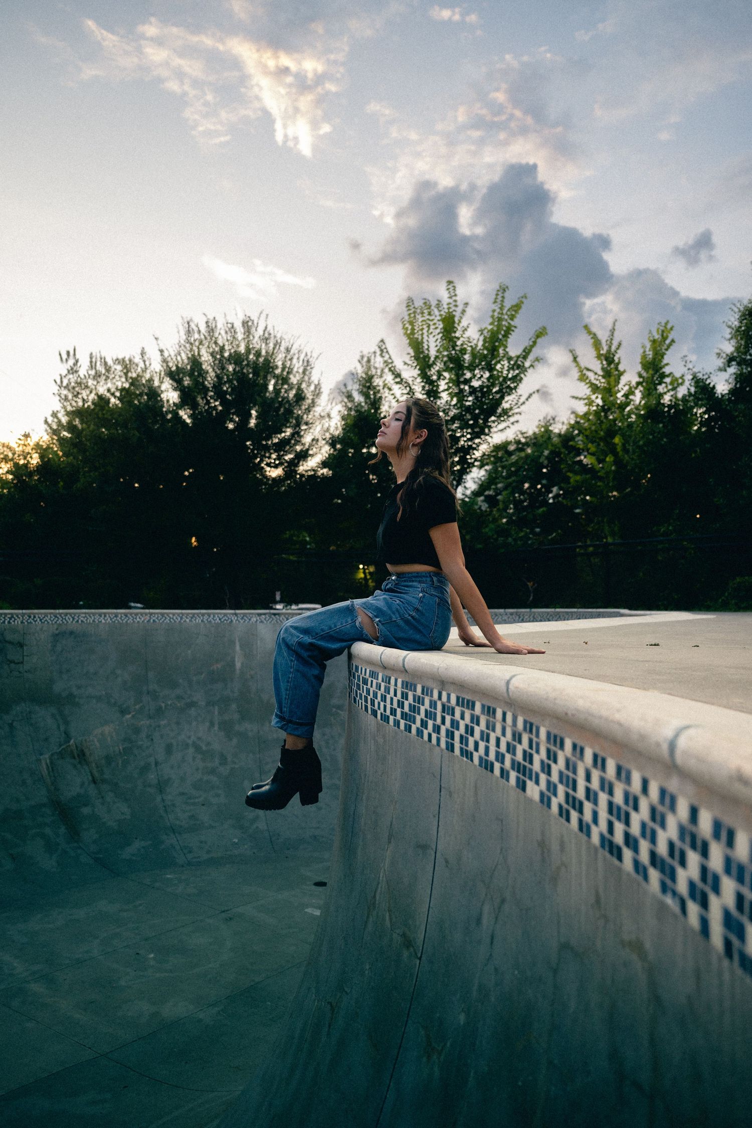 Dramatic sunset silhouette of someone reclining on a curved concrete wall with decorative tile border.