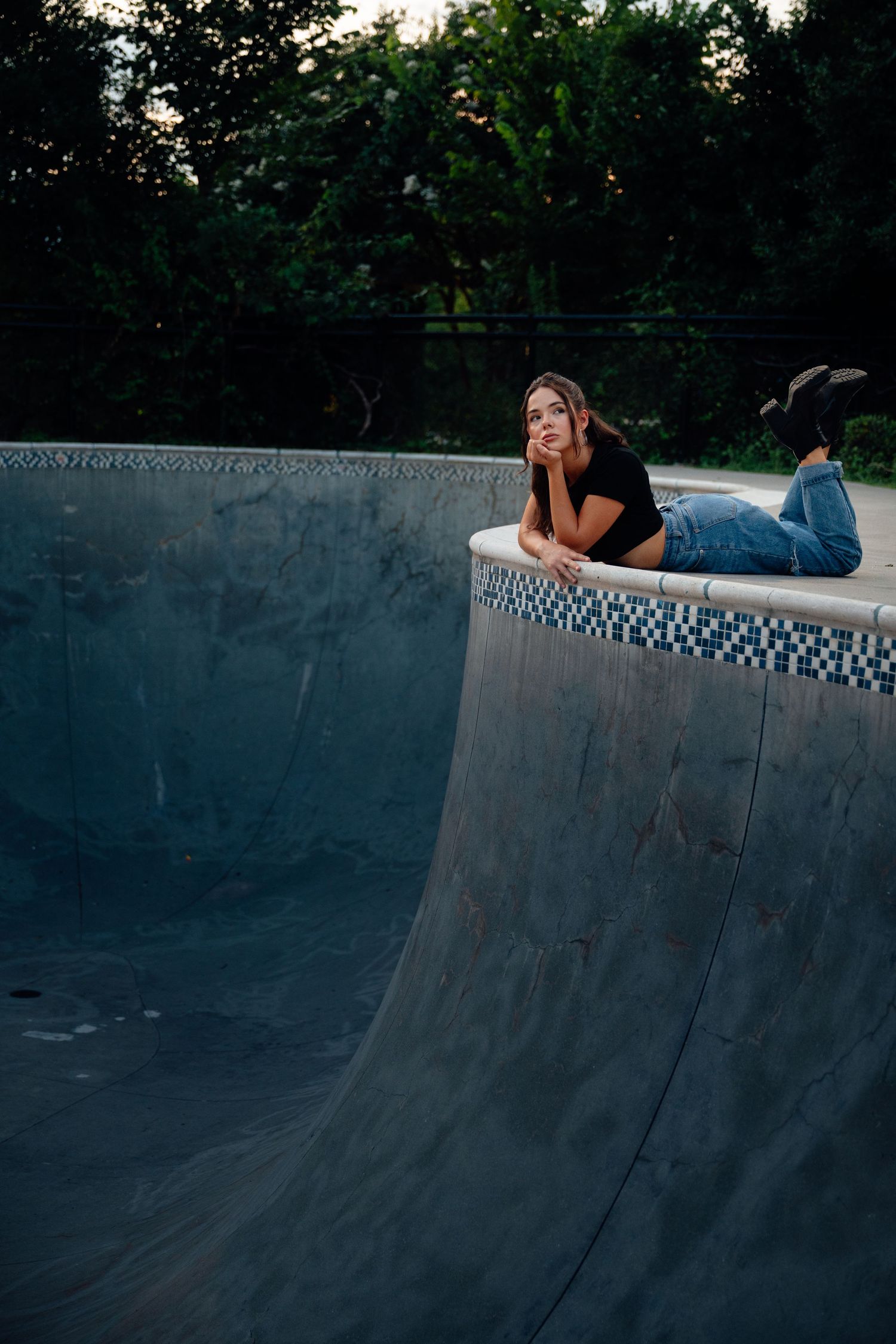 Person lying casually on curved concrete structure at dusk with trees in background.