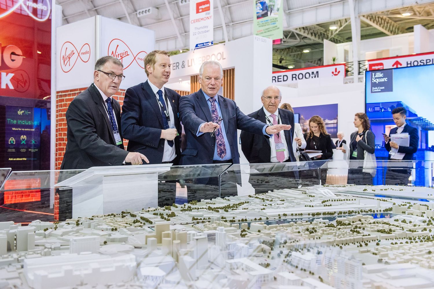 Exhibition space with architectural model display and company logos on white walls.