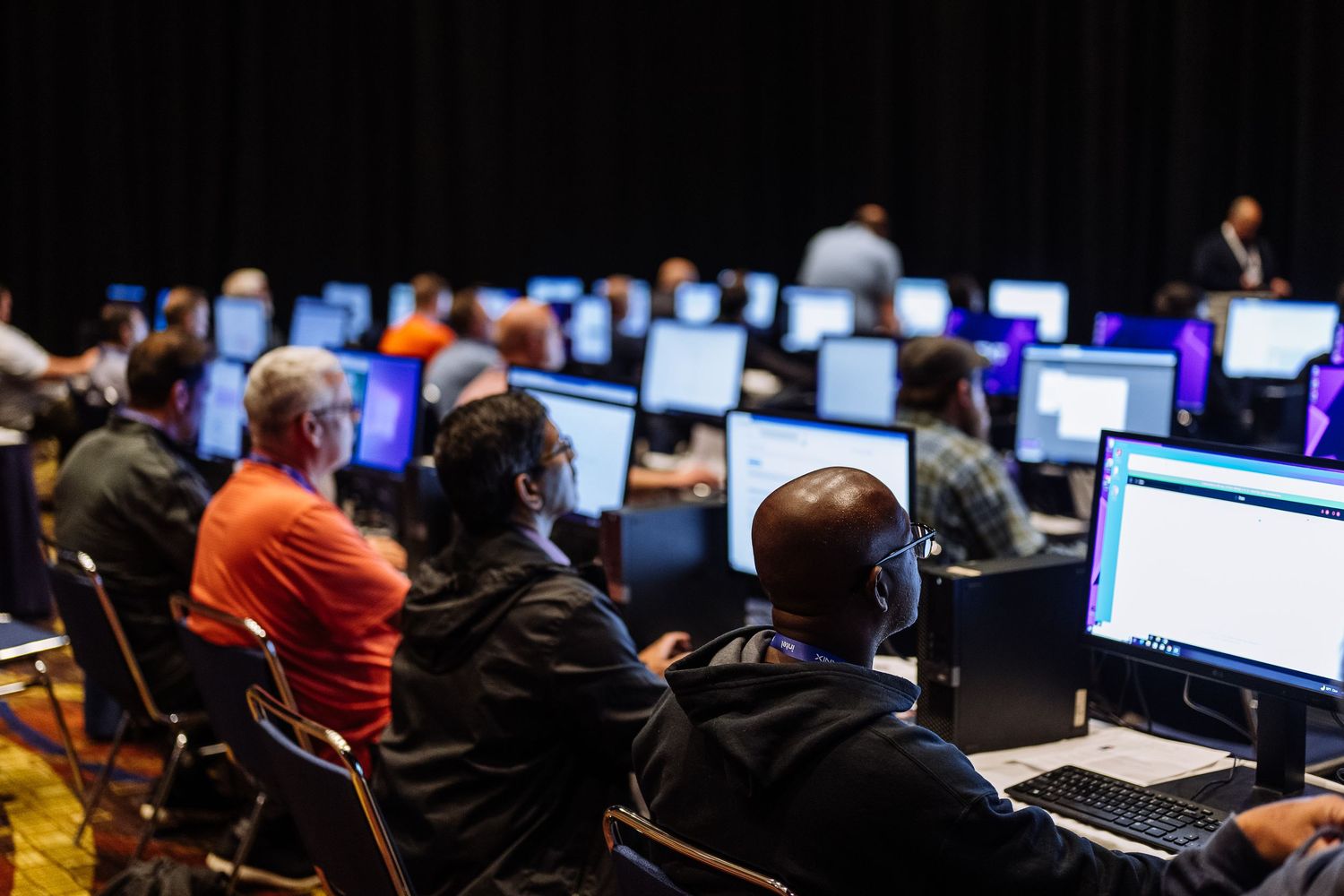 Dark room filled with computer workstations and monitors in rows.