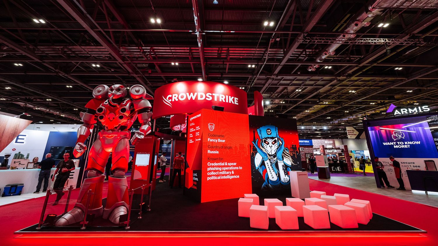 Wide panoramic view of a technology conference exhibition hall with red lighting and vendor booths.