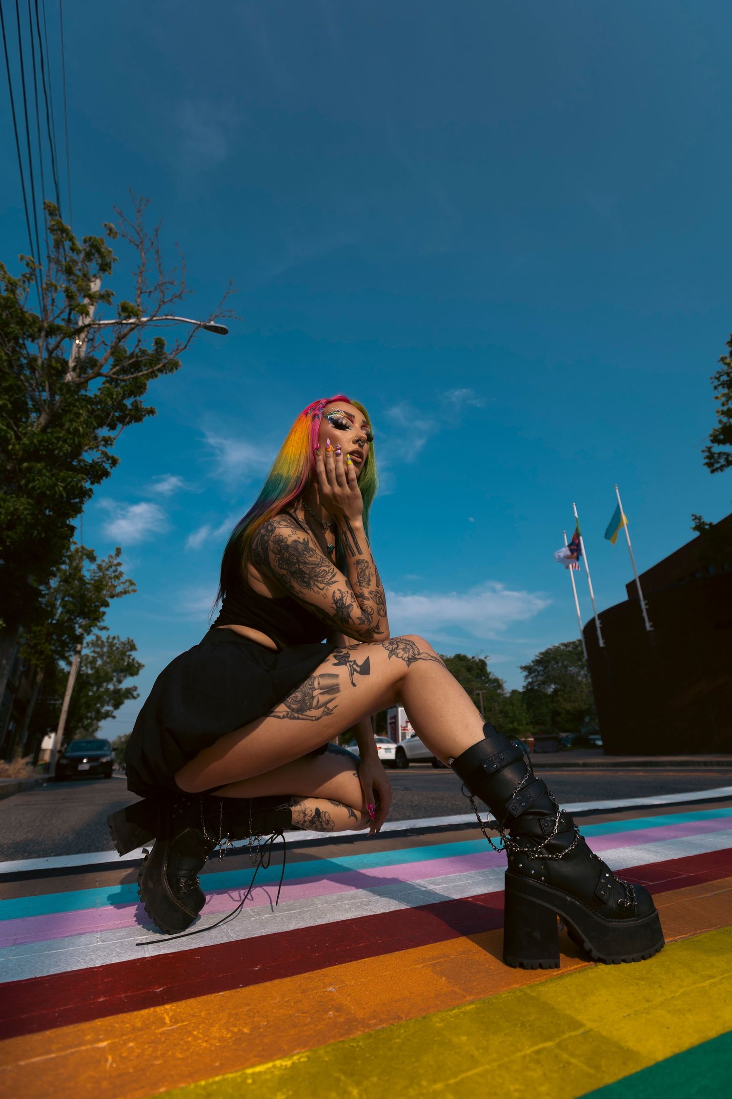 A person wearing combat boots sits on a colorful rainbow painted surface under a blue sky.