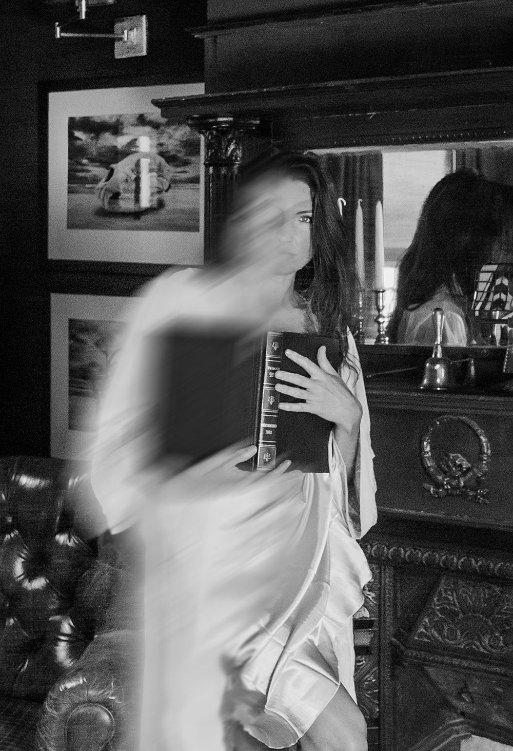 A blurred motion black and white photograph captures a ghostly figure in white moving through a dimly lit interior space.