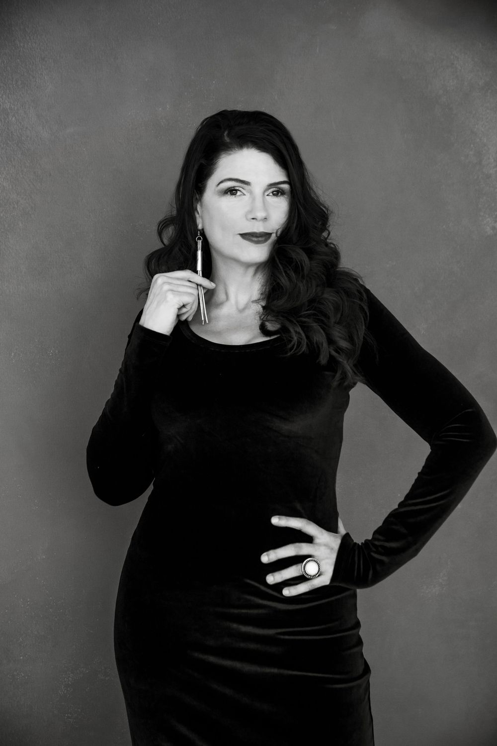 Elegant monochrome portrait of a fashionable woman in a black velvet dress posing against a dark background.