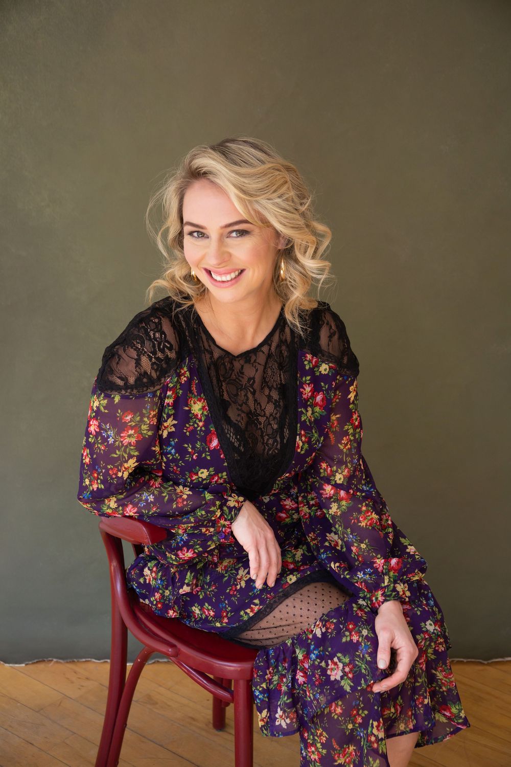 A floral dress-clad figure poses playfully on a wooden chair against a dark backdrop in a series of candid shots.
