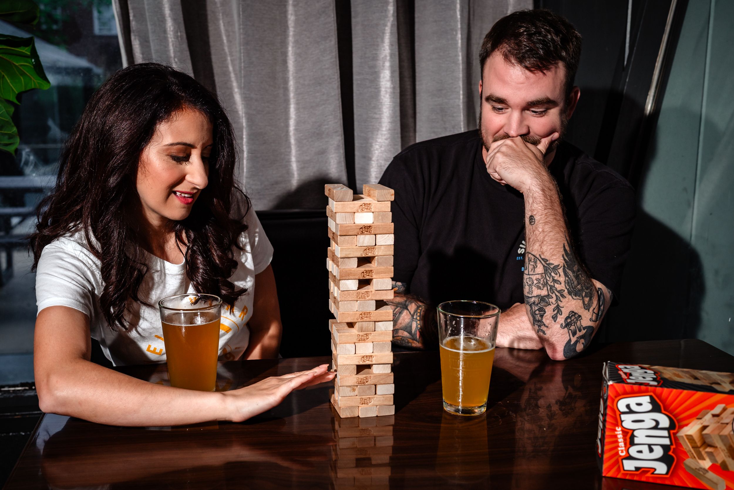 Couple playing Jenga at a bar with drinks while enjoying a fun evening together.