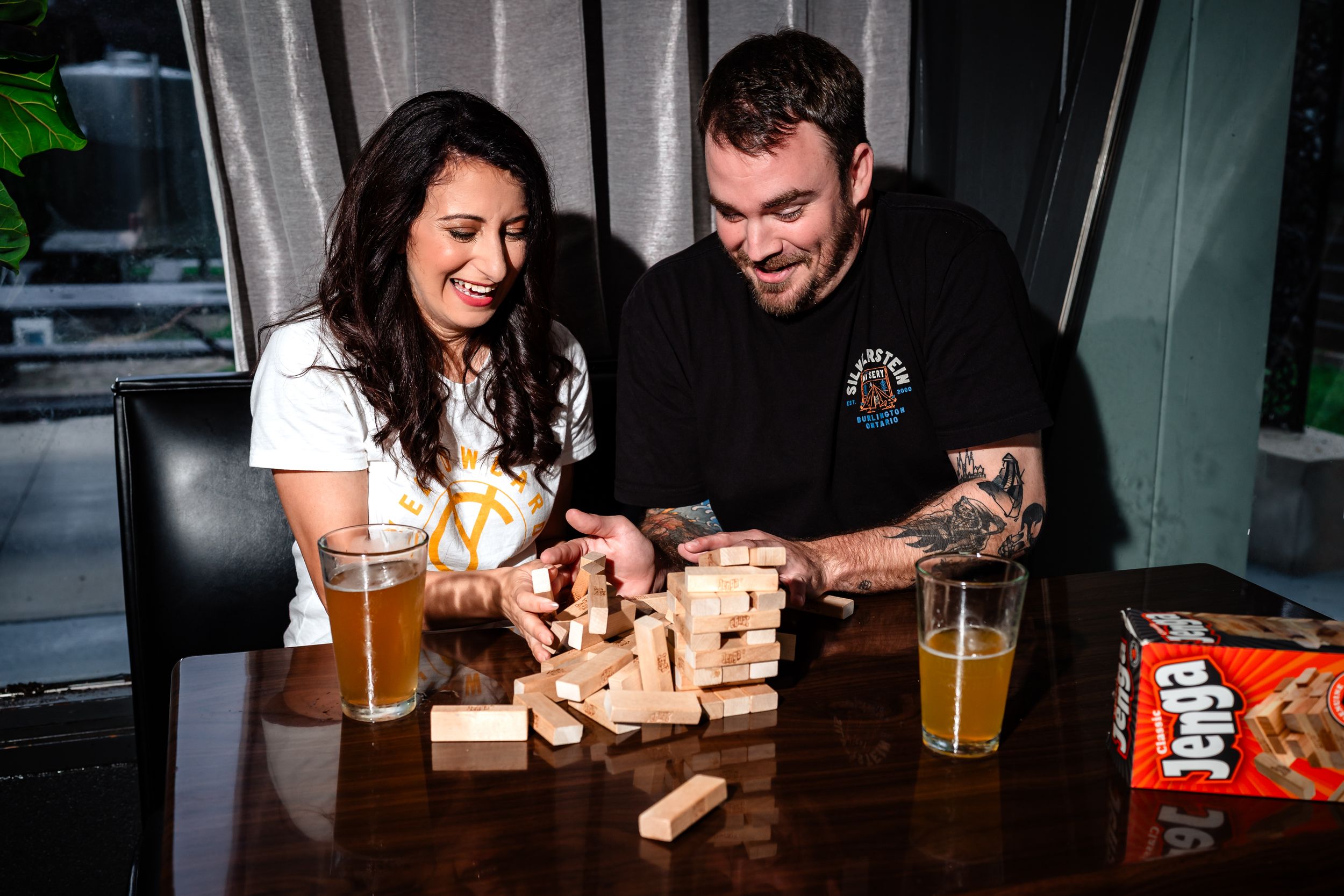 Players carefully removing wooden blocks from a Jenga tower during an intense game at a bar.