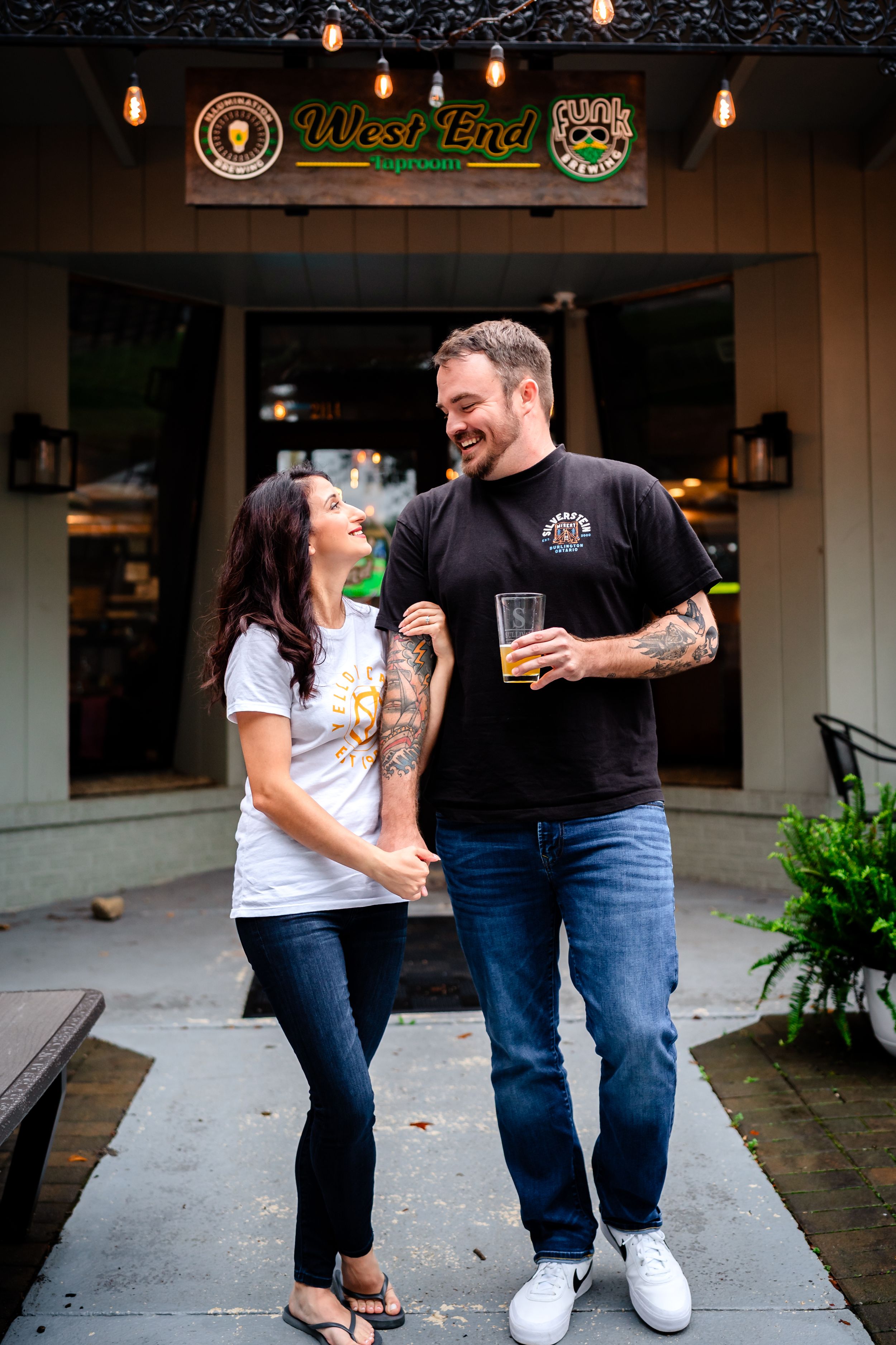Couple sharing playful moments outside a bar with string lights overhead.