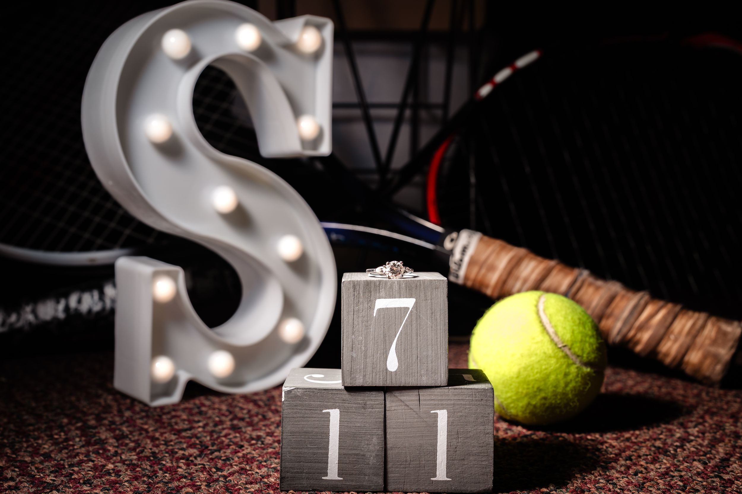 Tennis balls and decorative light up letters create a romantic engagement photo setup on a dark background.