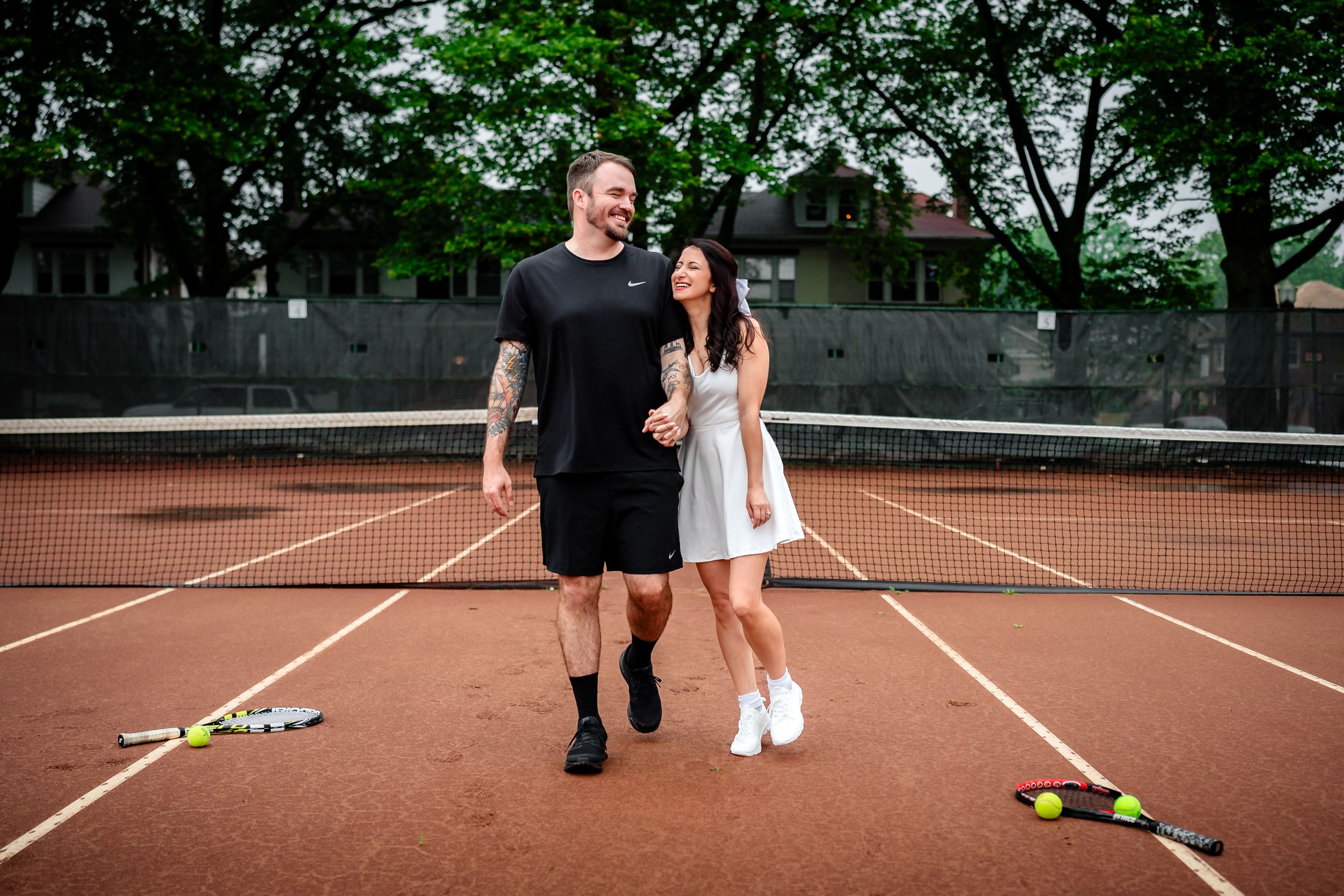 A tennis court engagement photoshoot with props scattered across the clay court surface.