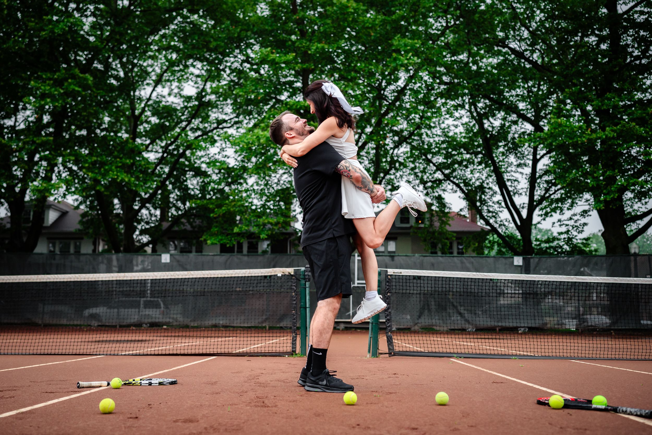 Tennis balls and rackets arranged artistically on a clay tennis court during sunset.