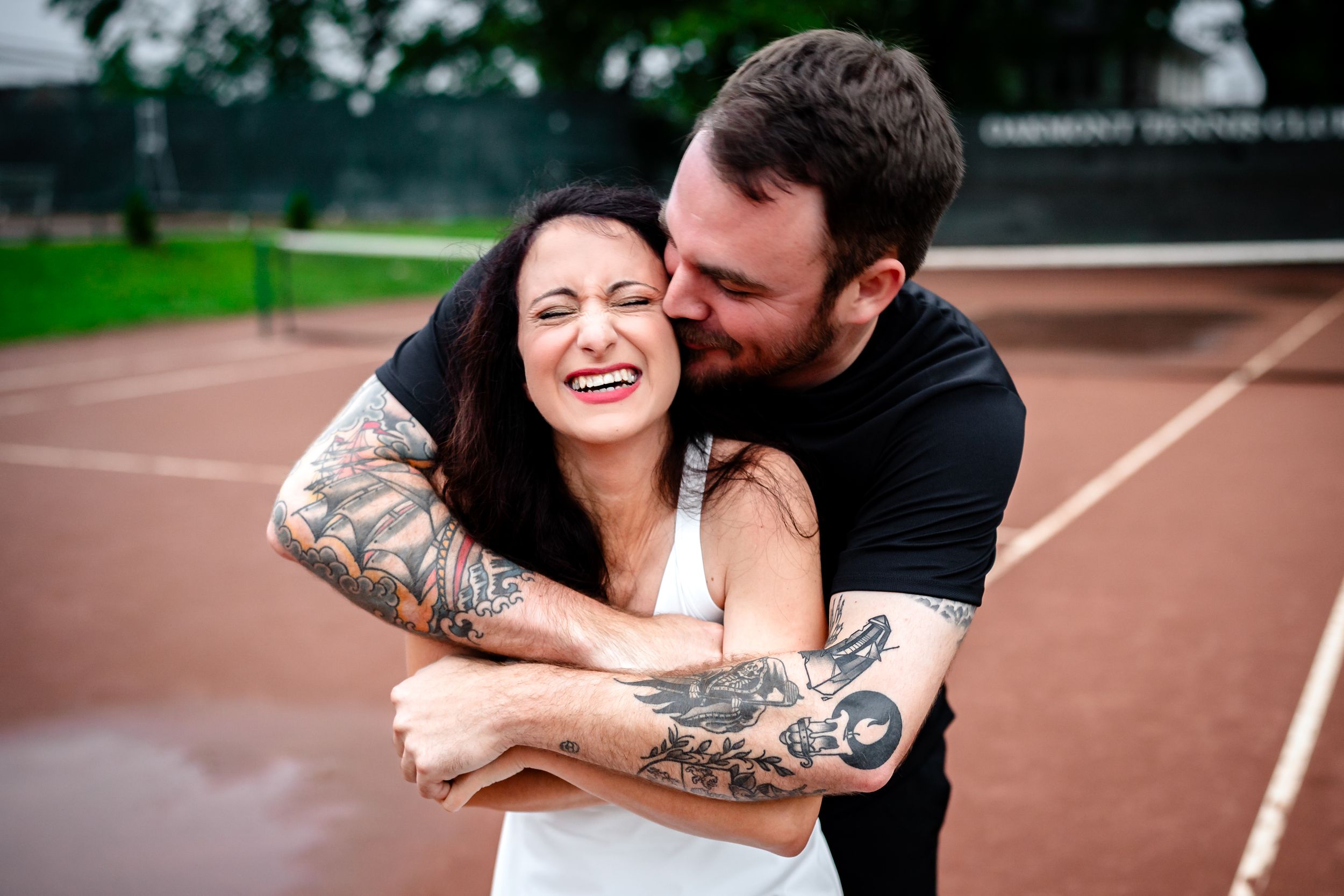 A playful moment captured during an engagement photoshoot on a tennis court.