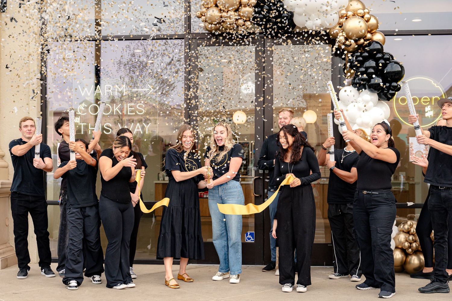 Group celebration with black and gold balloons and confetti in an urban setting.