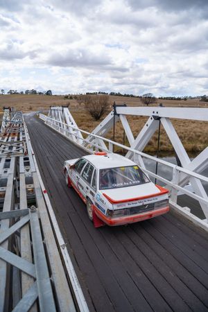 A vintage white and red car parked on a wooden bridge with cloudy skies in the background.