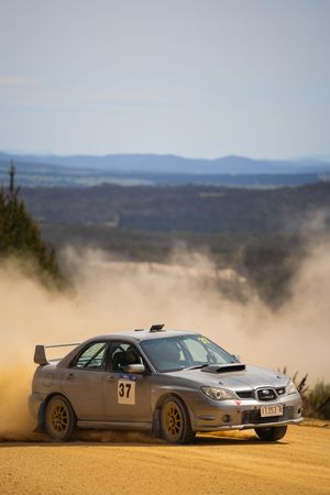 Silver sports cars kick up dust while racing on a dirt track with mountains visible in the background.
