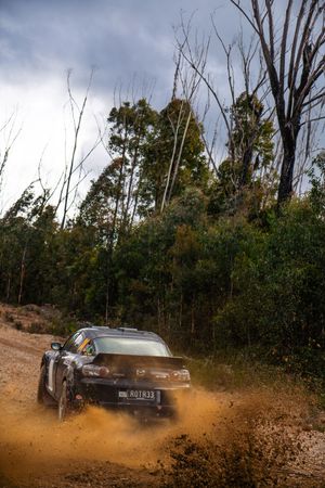 A black BMW rally car kicks up dirt and mud while drifting through a challenging off-road course.