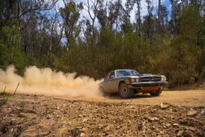 Classic muscle car sliding through dirt track creating dramatic dust clouds.