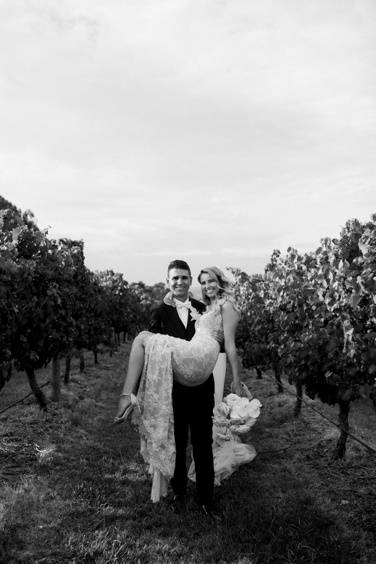 Black and white photo of couple walking through vineyard rows.