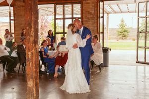 A wedding couple shares their first dance in a rustic venue with wooden beams and large windows overlooking scenic grounds.