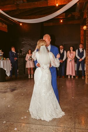 A couple shares their first dance at their rustic barn wedding reception with guests watching in the background.