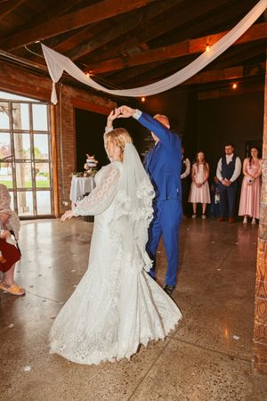 A couple performs an elegant twirl during their wedding dance in a rustic venue with draped fabric decor.