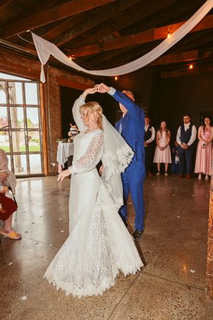 Couples dancing during a wedding reception in a rustic barn venue with wood beams and white decorations.