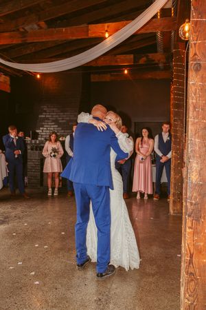 A couple shares their first dance in a rustic brick venue decorated with white drapes and string lights.