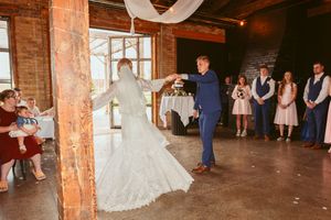 Couple spins during their first dance at a rustic wedding venue with exposed brick walls and white draping.