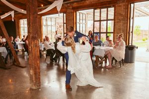 Newlyweds performing their first dance in a sunlit barn venue while guests watch from tables.