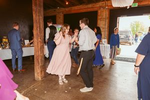 Wedding guests mingle and dance in a rustic wooden barn venue during an evening celebration.