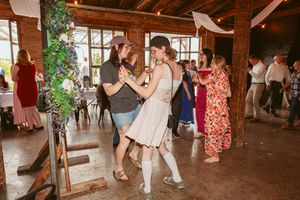 Wedding guests dancing together in a rustic barn venue with natural lighting streaming through windows.