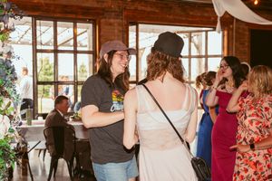 People gathered at an indoor rustic venue with wooden beams and large windows for a social event.