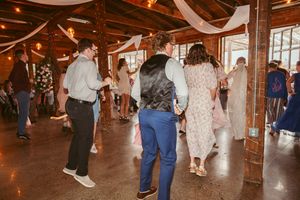 People dance at a rustic barn wedding reception with wooden beams and warm lighting.