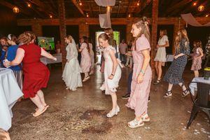 Wedding reception guests dancing and enjoying themselves on a rustic barn dance floor with string lights overhead.