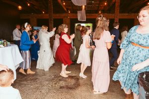 Wedding guests dancing and celebrating on the rustic reception venue floor with string lights overhead.