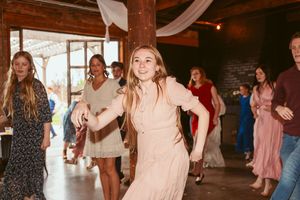 Wedding party and guests enjoying a dance celebration in a rustic wooden barn interior.