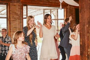 Wedding guests dancing and celebrating in a rustic venue with large windows and wooden beams.