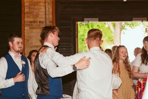 Guests in formal attire dance together at a rustic wooden barn venue during a celebration.