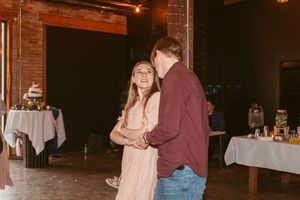 Couple dancing together at a reception in a dimly lit brick venue with tables in the background.